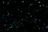 Dark glitter or stars of white, green and blue colors over dark background with copy space