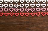 Romantic border of colored hearts in white pink and red arranged in rows on a textured wooden background with copy space