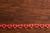 Line of foam heart shapes near bottom of dark wooden panel as background with copy space
