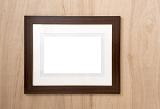 Empty dark wood simple frame with inner neutral colored mount card hanging on a wooden wall