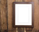 Single empty simple wooden frame with plain white mount card hanging on a wooden background with space for your artwork or photo