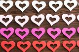 Wooden hearts background with modern cut outs arranged in four rows graduating from white through pink to red on wood symbolic of love and romance