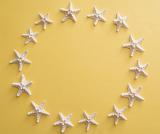 Decorative circular frame of dried white starfish on a yellow background with copy space for marine or nautical themes