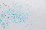 Scattered pieces of blue and green glitter sprinkled on gray paper as background