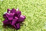 Holiday or gift concept of shiny purple bow in corner of green sparkling glitter background with copy space