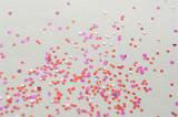 Scattered pieces of red and pink glitter sprinkled on gray paper as background
