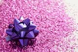 Celebratory Full Frame Background of Sparkling Pink Glitter and Shiny Metallic Purple Gift Bow in Bright Studio with Selective Focus and Copy Space