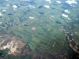 High angle airplane view of cultivated land and waterways with clouds above and reflective swamp