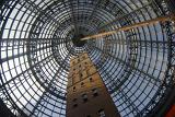 Tall shot brick tower within a glass and steel beam dome from low angle view under bright sky