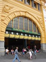 Ornate arched entrance to Flinders Street Station, Melbourne, Australia, with people sitting on the steps and commuters making their way to and from the trains
