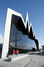 Distinctive modern exterior facade of the Riverside Museum, Glasgow. Scotland with its zigzag design and large window reflecting a tall ship in the harbour
