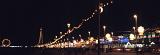 Night panorama of beachfront illumination in Blackpool with colorful lights stretching around the promenade above the beach and the outlines of the Blackpool Tower and pier with its ferris wheel