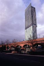 Architecture in central Manchester with a tall modern skyscraper towering above a historic arched railways bridges