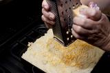 Grating cheese over the mashed potato topping on a cottage pie before place it in the oven to bake or grill