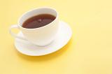England marches on cups of tea: Freshly brewed cup of hot refreshing black tea served in a white cup and saucer on a pale yellow background with copyspace