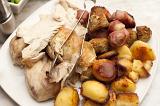 Carved roast chicken, roast potato and vegetables on a plate with metal thongs ready to be served for dinner