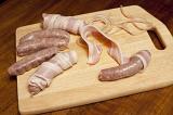 Making bacon rolls with spicy sausages wrapped in rashers of cured bacon laid out on a wooden board in the kitchen
