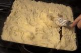 Preparing Shepherds pie in the kitchen smoothing the mashed potato topping or crust over the minced meat with a fork, close up view of the oven dish