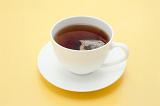 Teabag steeping in a cup of fresh hot tea to obtain the desired strength of the brew in a plain white cup and saucer on a yellow background