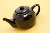 Brown glazed ceramic teapot for brewing a fresh cup of hot tea on a pale yellow background, high angle view