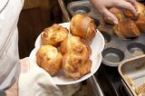 Removing a batch of delicious light puffy Yorkshire Puddings from a baking tray onto a warm plate in preparation to serve them with a dinner of traditional roast beef