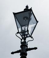 Old Victorian gas streetlamp with its wrought iron lantern against a dull grey sky, close up detail