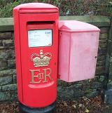 Traditional red Royal Mail post box on a street alongside a stone wall in Great Britain