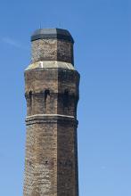 Top of an old industrial brick chimney or smokestack with hexagonal design against a clear blue sky