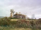 Skyline view of an industrial production plant against a cloudy sky viewed over bushes and scrub