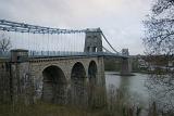 Menai suspension bridge on the Isle of Anglesey, Wales on an overcast cloudy day viewed from the bank