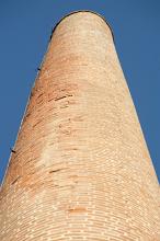 Old cylindrical red brick industrial chimney or smokestack at a factory looking up from below to blue sky