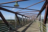 View along a pedestrian and cycle crossing on an old steel bridge with open framework under a blue sky