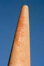 Old red brick industrial chimney viewed from below rising against a blue sky