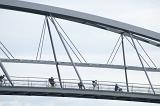 People walking and cycling across a pedestrian bridge silhouetted against a high key sky in a structural engineering and architecture concept