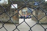 Looking through a school fence at a distant group of students gathered in a courtyard