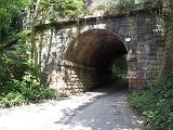 Road passing through an arched underpass or tunnel under a road above in a shady green country lane