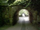 Pass under the arch through an old thick stone wall with green foliage