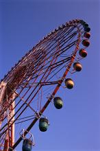 Looking up at the rim and gondolas of a Big Wheel at an amusement park or fairground against a blue sky