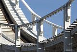 A close up of a white roller coaster track and railing with a blue sky background.