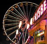 Brightly lit stalls and illuminated ferris wheel at a fairground or amusement park at night in a close up view