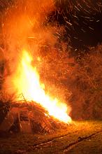 Roaring bonfire with flying embers alongside a rural track shooting fiery orange flames into the night sky