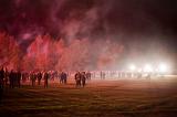 Spectators at a Bonfire Night event gathered in an open field in smoke filled air from the exploding fireworks