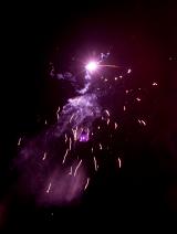 Colourful display of purple fireworks with sparks and light trails cascading down from a rocket high in the dark night sky during a festive occasion
