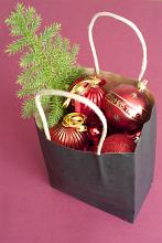 Paper bag filled with colourful Christmas decorations with red baubles and a small pine Xmas tree over a red background