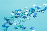 Still Life of Blue and Silver Stars Scattered Across Teal Colored Background with Copy Space