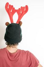Rear view of a person wearing a colorful red reindeer Christmas hat with antlers facing a white wall with copy space