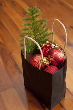 Recyclable paper carrier bag filled with colorful red with Christmas decorations and a small green pine tree to decorate on a wooden floor