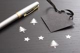 Dark grey Christmas label with fountain pen and scattered decorations on a textured dark wood background