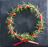 Homemade Christmas wreath with rosemary foliage and a twisted red ribbon over a textured dark background with copy space