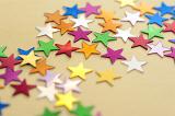 Colorful stars background with numerous, multicolored stars scattered across a festive yellow background viewed low angle with shallow dof